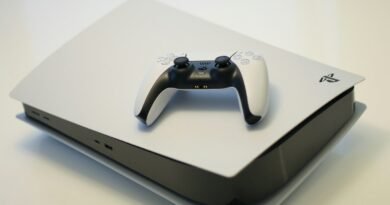 A white game console with a matching wireless controller on a white su