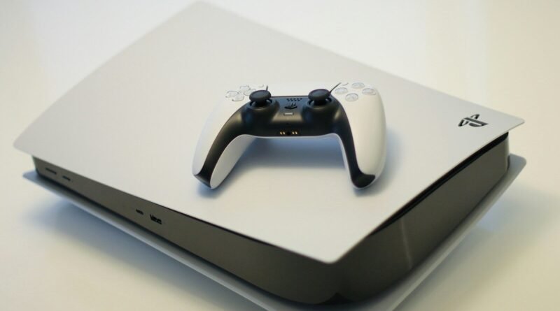 A white game console with a matching wireless controller on a white su